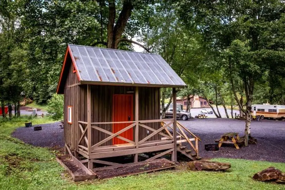 Rustic family cabin on a gravel RV site with picnic table and fire pit – Partial Hookup RV with Rustic Family Cabin at The Outpost NRG
